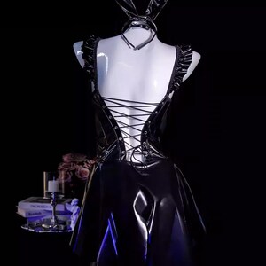 May include: Black faux leather bunny costume with a halter top, ruffled shoulder straps, and a lace-up back. Includes a matching choker and bunny ears. The dress has a flared skirt.