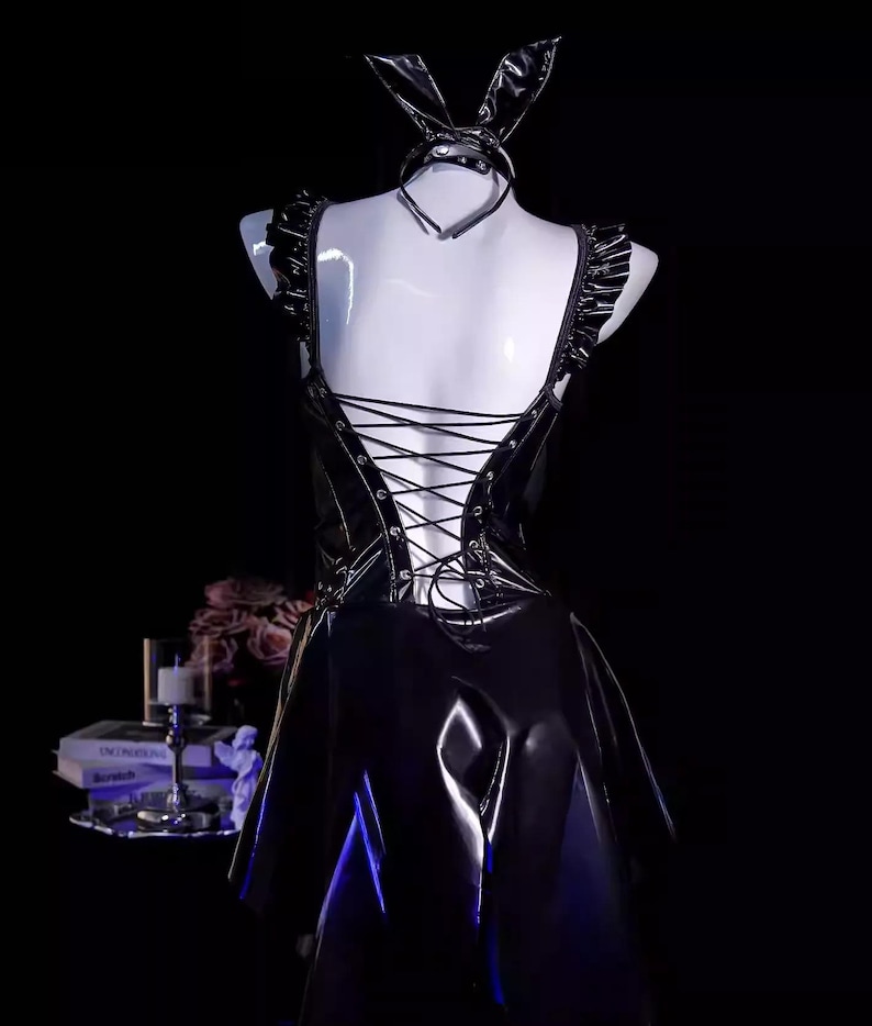 May include: Black faux leather bunny costume with a halter top, ruffled shoulder straps, and a lace-up back. Includes a matching choker and bunny ears. The dress has a flared skirt.