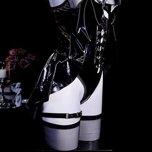 May include: Black patent leather bodysuit with lace-up detailing and a garter belt. The garment has a shiny, reflective surface and is displayed on a mannequin. The background is dark, emphasizing the product's sleek design.