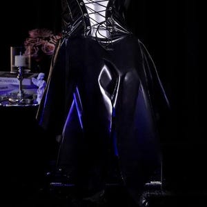 May include: A black, shiny, vinyl-like garment with a lace-up bodice and a flowing skirt. The garment is displayed in a dimly lit setting, with a hint of blue light illuminating the folds of the fabric. The overall aesthetic is gothic and edgy.
