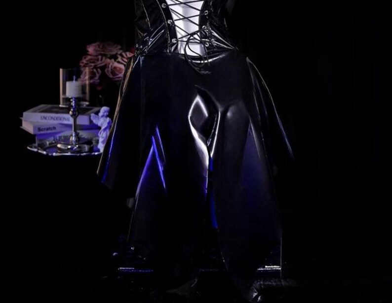 May include: A black, shiny, vinyl-like garment with a lace-up bodice and a flowing skirt. The garment is displayed in a dimly lit setting, with a hint of blue light illuminating the folds of the fabric. The overall aesthetic is gothic and edgy.