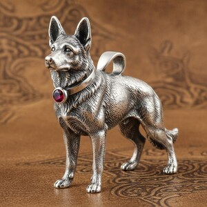 May include: A silver pendant depicting a German Shepherd dog. The dog has a collar with a red gemstone. The pendant is detailed with realistic fur and has a loop for a chain.