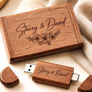 May include: A rectangular wooden box and a matching USB flash drive with a metal connector. Both items feature the engraved text "Stacey & David" in a cursive script. The box lid also displays an engraved floral design below the names.