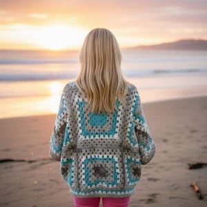 Peut inclure: Un cardigan crocheté à la main, avec des carrés granny gris, turquoise et blancs. Le pull sans fermeture est porté par une personne sur une plage au coucher du soleil. Le cardigan est un vêtement confortable et élégant.