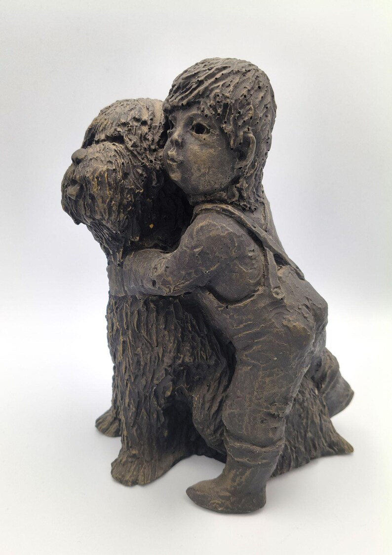 Puede incluir: Una escultura texturizada de color marr&oacute;n oscuro que representa a un ni&ntilde;o con peto abrazando a un perro de pelo peludo. La figura muestra al ni&ntilde;o con los brazos alrededor del cuello del perro, capturando una interacci&oacute;n cercana.