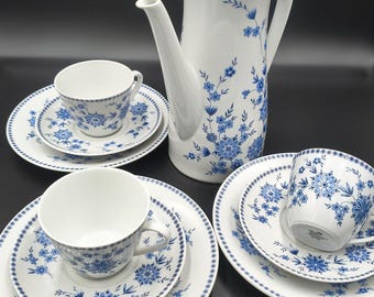 May include: A white porcelain tea set with blue floral patterns. The set includes a tall coffee pot, cups, saucers, and plates. The rims of the plates and cups have a dotted border.