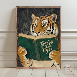 Puede incluir: Impresión artística enmarcada de un tigre leyendo un libro. El tigre, con rayas naranjas y negras, tiene una expresión concentrada. El libro es verde con la inscripción dorada "Go Get 'Em Tiger". El fondo presenta un diseño floral oscuro.