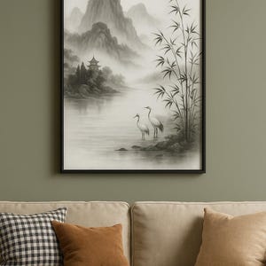 Op de afbeelding: Zwartgelijste kunstdruk met een serene Aziatische landschap. Het kunstwerk toont een mistige bergketen, een pagode en twee witte vogels bij bamboestengels. Het kleurenpalet is voornamelijk grijs met zachte, gedempte tinten.
