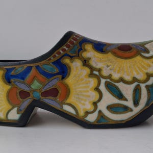 May include: A ceramic clog-shaped planter with a black base and intricate floral designs. The planter features yellow, blue, orange, and green patterns with a cream-colored background. The decorative piece is a unique home decor item.