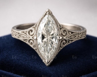 May include: A marquise-cut diamond ring with an engraved band. The ring features a large, clear diamond set in a detailed, vintage-style setting. The silver-toned band has intricate scrollwork and bead detailing, creating a classic and elegant look.