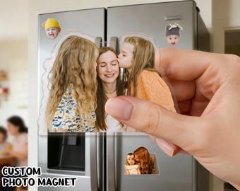 Può includere: Un magnete fotografico personalizzato, trasparente e rettangolare, tenuto in mano, con una foto di famiglia di una madre e due figlie. Il magnete è esposto su un frigorifero in acciaio inossidabile. Sono attaccati anche altri magneti fotografici. Il testo "CUSTOM PHOTO MAGNET" è visibile.