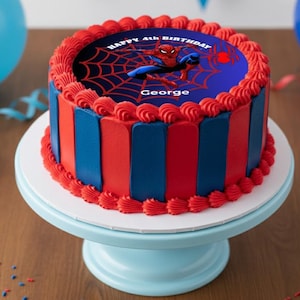 Könnte beinhalten: Ein runder Geburtstagskuchen mit roter und blauer Glasur, verziert mit einem Spider-Man-Bild und dem Text "HAPPY 4th BIRTHDAY GEORGE". Der Kuchen steht auf einer hellblauen Tortenplatte.