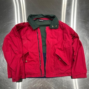 Puede incluir: Chaqueta Nautica roja con cuello verde y interior verde oscuro. La chaqueta tiene cierre de cremallera, dos bolsillos delanteros y el logo de Nautica en el cuello. La chaqueta es de talla mediana.