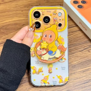 Puede incluir: Funda transparente para teléfono con borde amarillo y diseño de dibujos animados. La funda presenta un bebé vestido de amarillo montado en un balancín y sosteniendo una estrella. Personajes de dibujos animados y estrellas adicionales están dispersos. El texto "Little Star" también es visible.
