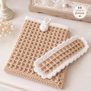 Peut inclure: Une pochette rectangulaire en crochet beige avec une texture en point gaufré et une bordure blanche. Elle présente une fermeture à bouton blanc avec une boucle. Un dessous de verre ovale assorti en crochet à bord festonné est posé dessus.