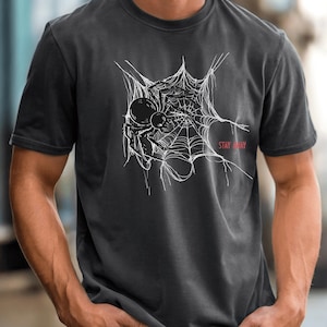 A man in a dark gray t-shirt with a white spider web and black spider graphic on the chest, with the words "STAY AWAY" in red.