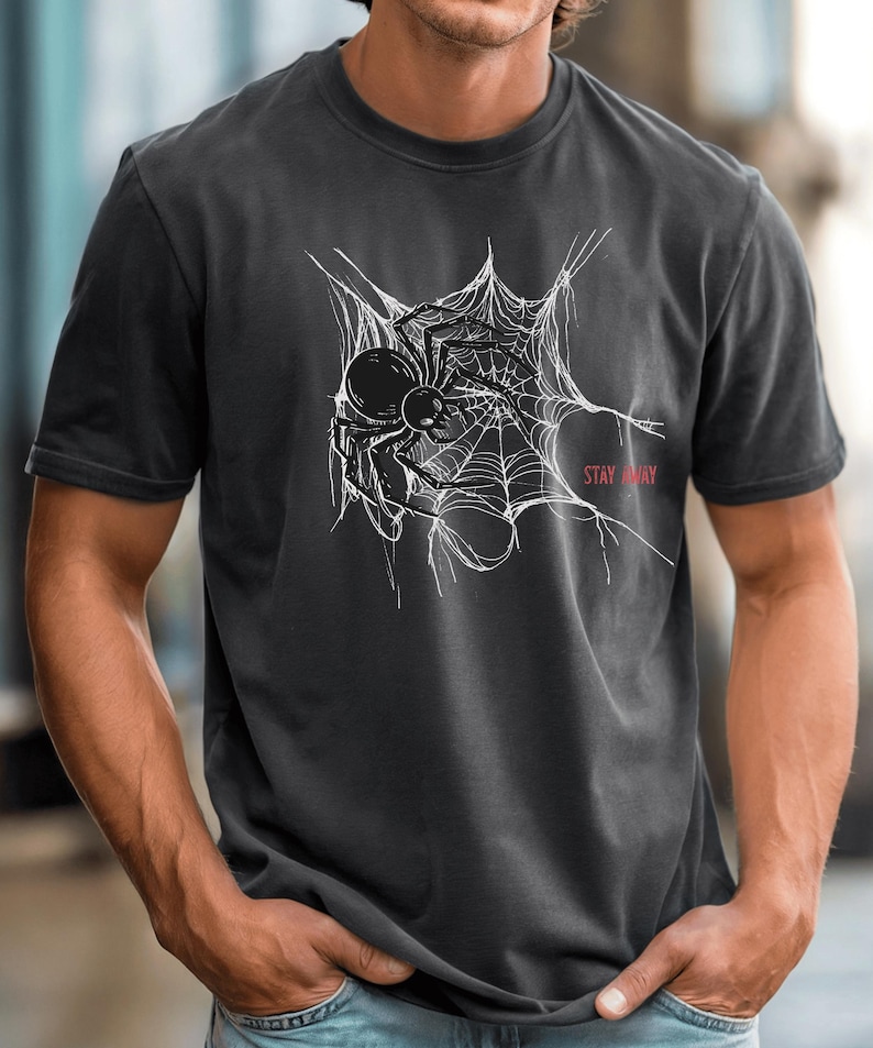 A man in a dark gray t-shirt with a white spider web and black spider graphic on the chest, with the words "STAY AWAY" in red.