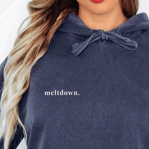 Close-up of the front of the dark blue hoodie showing the word meltdown in small white lowercase letters on the right chest area.