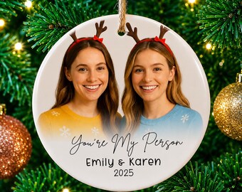 May include: A round white ceramic Christmas ornament featuring a photo of two smiling individuals wearing reindeer antler headbands. The text reads You're My Person, Emily & Karen, and 2025. The ornament hangs from a rustic twine loop.