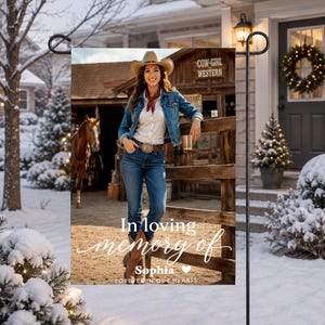 May include: A rectangular garden flag featuring a photograph of a person in a cowboy hat, denim jacket, and jeans leaning against a wooden fence near a horse. The text reads In loving memory of Sophia FOREVER IN OUR HEARTS.