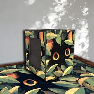Peut inclure: Boîte et tapis avec un motif de chat noir caché dans des feuilles vertes et jaunes. Le chat a de grands yeux jaunes et des oreilles orange. La boîte a une ouverture grise foncée.