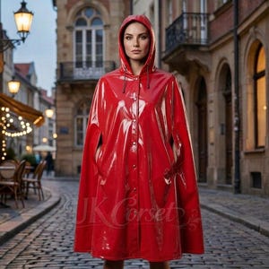 May include: A bright red hooded raincoat with a glossy finish. The coat has a button-up front and pockets. The image is taken outdoors on a cobblestone street, with the text "UK Corset" visible on the coat.