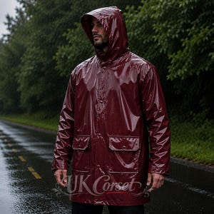 Puede incluir: Un impermeable de color burdeos oscuro brillante con capucha, mangas largas y dos bolsillos delanteros con solapas abotonadas. La chaqueta tiene un cierre central de botones y un acabado liso y reflectante. El texto UK Corset es visible abajo.