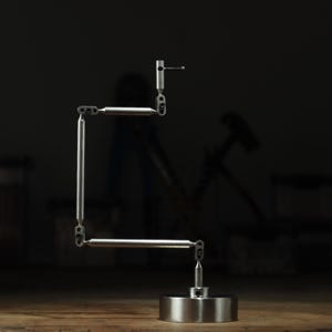 May include: A silver metal desk lamp with a circular base and a series of articulated arms and springs. The lamp is designed to be adjustable. The background is dark, with a wooden surface in the foreground.