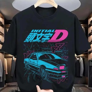 Puede incluir: Camiseta negra con un gráfico en azul neón y rosa de un coche deportivo en una carretera sinuosa. El diseño incluye el texto "INITIAL D" en azul y rosa, con caracteres japoneses. El coche está detallado con detalles en azul neón y rosa.