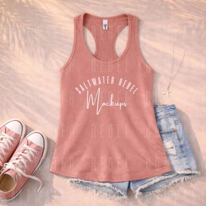 Puede incluir: Una camiseta sin mangas de color coral con el texto "Saltwater Rebel Mockups" en blanco, combinada con pantalones cortos de mezclilla, zapatillas rosas y un collar plateado. La camiseta sin mangas tiene un diseño de espalda deportiva. Los pantalones cortos están desgastados.