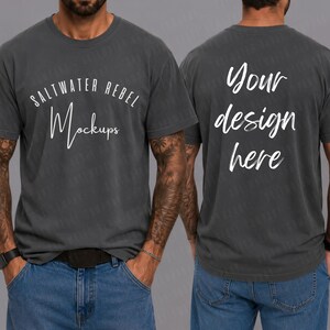 May include: Dark grey t-shirt featuring the text "SALTWATER REBEL Mockups" on the front and "Your design here" on the back. The t-shirt is a crew neck style and is worn with blue jeans.