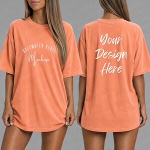 May include: A coral-colored oversized t-shirt with short sleeves. The front of the shirt features the text "Saltwater Rebel Mockups" in white script. The back of the shirt displays the text "Your Design Here" in white script.
