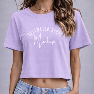 Może przedstawiać: Jasnofioletowy crop top z białym napisem "SALTWATER REBEL Mockups". Koszulka ma krótkie rękawy i okrągły dekolt. Modelka ma na sobie niebieskie dżinsy.