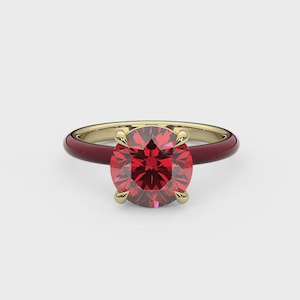 May include: A gold ring with a large, round, red gemstone. The band is a deep red color with a gold interior. The gemstone is held in place by four gold prongs.