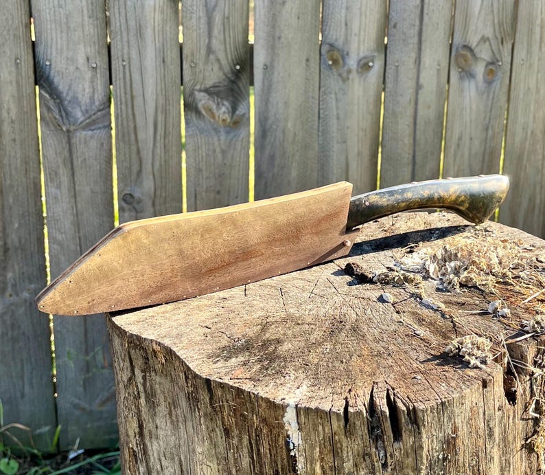 Puede incluir: Un cepillo de madera vintage con un mango de metal oscuro descansa sobre un toc&oacute;n de &aacute;rbol. El cuerpo de madera del cepillo es de un marr&oacute;n c&aacute;lido, y el mango tiene un aspecto deslustrado y envejecido. La herramienta est&aacute; dise&ntilde;ada para carpinter&iacute;a.