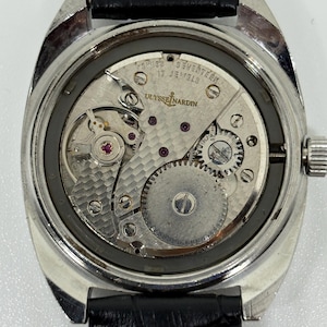 K&ouml;nnte beinhalten: Eine silberfarbene Armbanduhr mit abgenommenem Geh&auml;useboden, die das mechanische Uhrwerk freilegt. Das Werk ist mit Ulysse Nardin, Swiss und Seventeen 17 Jewels graviert. Sie hat ein schwarzes Lederarmband mit wei&szlig;en Ziern&auml;hten.