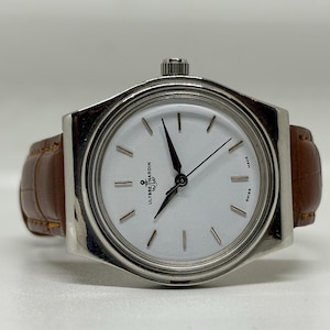 May include: A silver-tone wristwatch with a round white dial, featuring black hands and hour markers. The dial displays the Ulysse Nardin logo with an anchor symbol. It is fitted with a brown leather strap with a textured, embossed pattern.