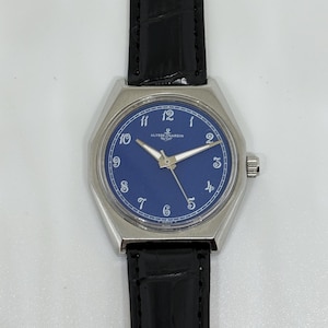 May include: A wristwatch with a silver-toned octagonal case and a deep blue dial featuring white Arabic numerals. The watch has silver-toned hands and a black leather strap with a textured finish. The Ulysse Nardin logo is printed on the dial.