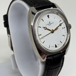 K&ouml;nnte beinhalten: Eine silberfarbene Armbanduhr mit wei&szlig;em Zifferblatt, goldfarbenen Zeigern und einem Anker-Logo mit dem Schriftzug ULYSSE NARDIN. Die Uhr hat ein schwarzes Lederarmband mit Strukturmuster und eine silberfarbene Krone an der Geh&auml;useseite.