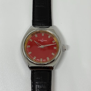 May include: A wristwatch with a circular silver-tone case, a vibrant red dial, and silver-tone hour markers. The dial features the text Ulysse Nardin and Swiss Made. It is attached to a black leather strap with a textured, crocodile-embossed finish.
