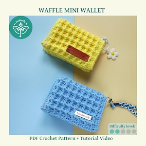 May include: Two crochet mini wallets with a waffle stitch texture, one in bright yellow and one in light blue. Each wallet features a small rectangular tag labeled handmade, a metal keyring, and a decorative charm attached to the side.