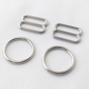 May include: Silver metal slider buckles and rings for sewing projects. The buckles are double-looped and the rings are round.