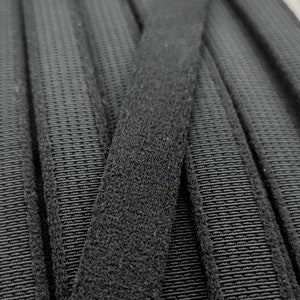 Könnte beinhalten: Schwarzes Klettband, auch bekannt als Velcro, mit einer strukturierten Oberfläche. Das Band ist in der Mitte gefaltet und zeigt beide Seiten des Materials.