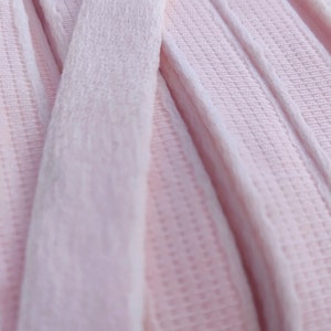 Könnte beinhalten: Nahaufnahme eines rosa Samtbandes mit einer strukturierten Oberfläche. Das Band ist gefaltet und übereinander gelegt, wodurch die weiche Textur des Stoffes sichtbar wird.