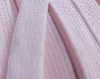 May include: Close-up of pink velvet ribbon with a textured surface. The ribbon is folded and layered, showing the soft texture of the fabric.