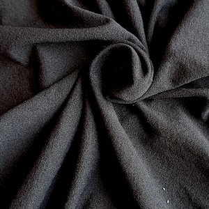 May include: Close-up of black fabric with a soft texture. The material is draped and folded, creating shadows and highlights. The fabric appears to be a knit or woven textile, suitable for clothing or home decor.