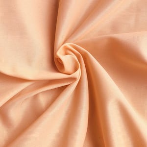 Könnte beinhalten: Eine Nahaufnahme eines pfirsichfarbenen Stoffes mit einer glatten, seidenartigen Textur. Der Stoff ist gefaltet und drapiert und erzeugt weiche, fließende Linien.