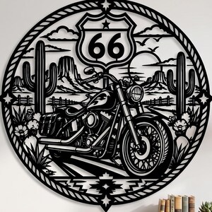 May include: A circular black metal wall art piece featuring a motorcycle in the foreground, a Route 66 road sign, desert landscape with cacti, mountains, and a sun in the background, all enclosed within a decorative rope-style border frame.