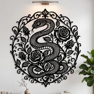 May include: Black metal wall art depicting a snake within a floral wreath of roses and leaves. The artwork is mounted on a white wall. The design is intricate and decorative, suitable for home decor. The piece is a striking contrast.