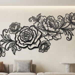 May include: Black metal floral wall art featuring roses and peonies. The decorative piece is mounted on a neutral-colored wall above a sofa. The design includes detailed leaves and swirling accents.